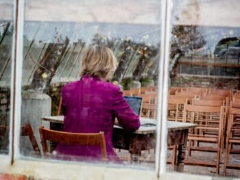 Esther van Wageningen werkt op haar laptop, met haar rug naar de camera, schrijvend over stressfysiologie en relaties.